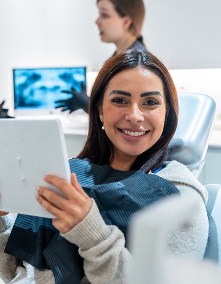 Patient smiling while holding mirror in treatment chair