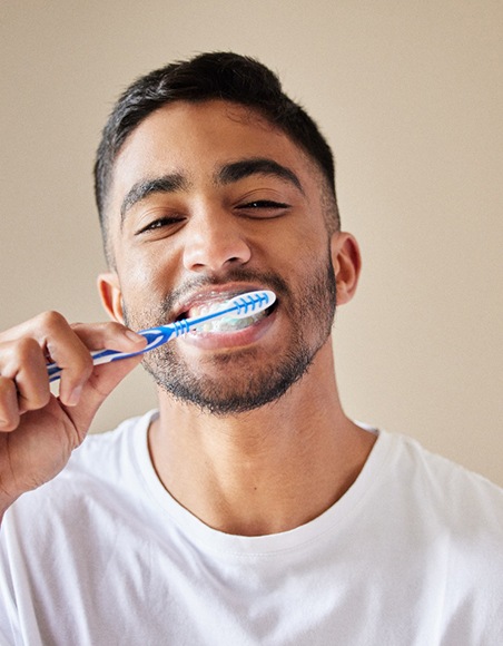 Smiling patient in white shirt brushing their teeth